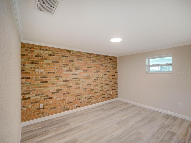 empty room with visible vents, wood finished floors, brick wall, crown molding, and baseboards