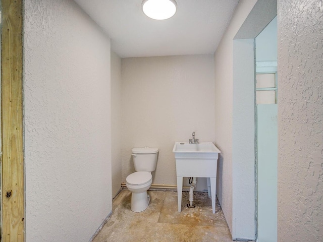 bathroom featuring unfinished concrete floors, toilet, and a textured wall