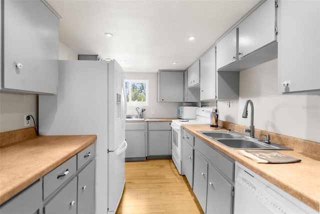 kitchen with light wood finished floors, gray cabinetry, a sink, white appliances, and light countertops