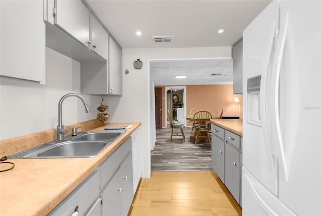 kitchen with visible vents, light wood finished floors, a sink, light countertops, and white fridge with ice dispenser