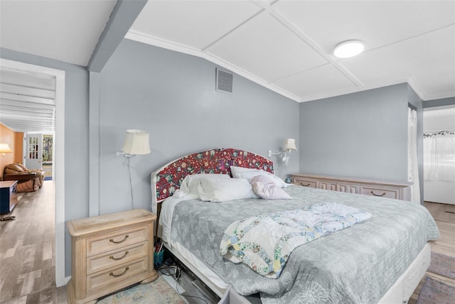 bedroom with vaulted ceiling, crown molding, wood finished floors, and visible vents