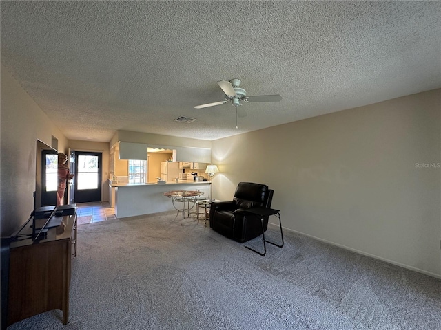 living area featuring ceiling fan, carpet floors, a textured ceiling, and visible vents