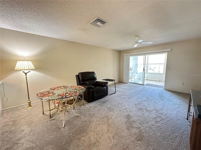 sitting room with carpet floors, visible vents, ceiling fan, and a textured ceiling