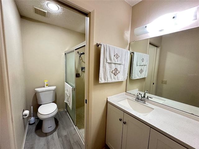 full bathroom with visible vents, toilet, a shower stall, a textured ceiling, and wood finished floors