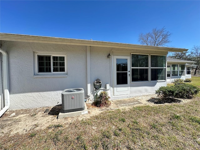 back of property with a sunroom, stucco siding, and central air condition unit