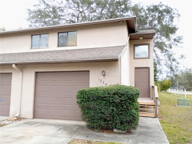 view of property with driveway, roof with shingles, an attached garage, and stucco siding