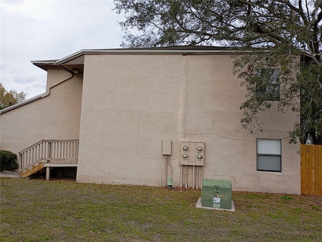 view of side of home featuring fence, a lawn, and stucco siding