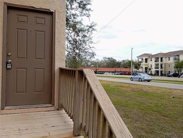 entrance to property with a residential view, a lawn, and stucco siding