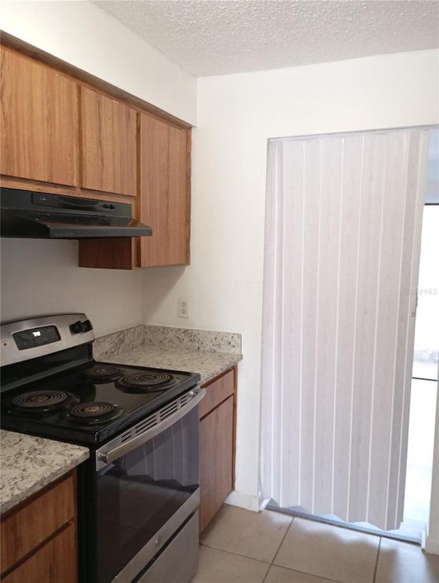 kitchen featuring light tile patterned floors, electric range, brown cabinetry, a textured ceiling, and under cabinet range hood