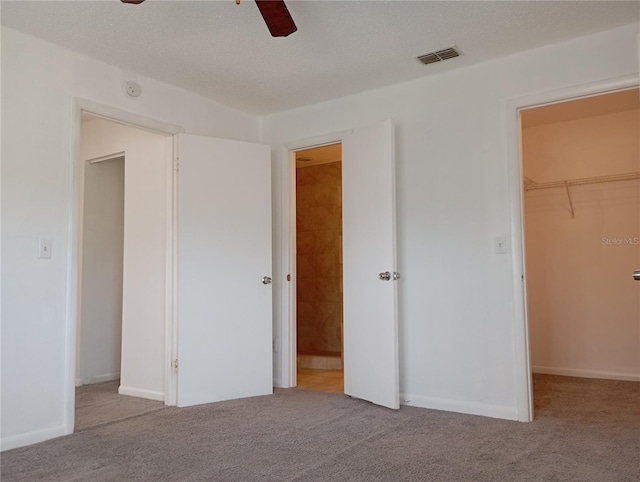 unfurnished bedroom featuring a textured ceiling, carpet floors, visible vents, a closet, and a walk in closet