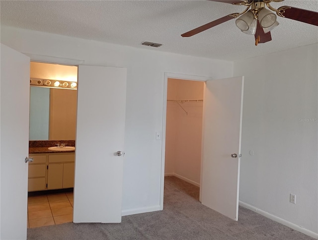 unfurnished bedroom featuring a textured ceiling, a spacious closet, a sink, and light colored carpet