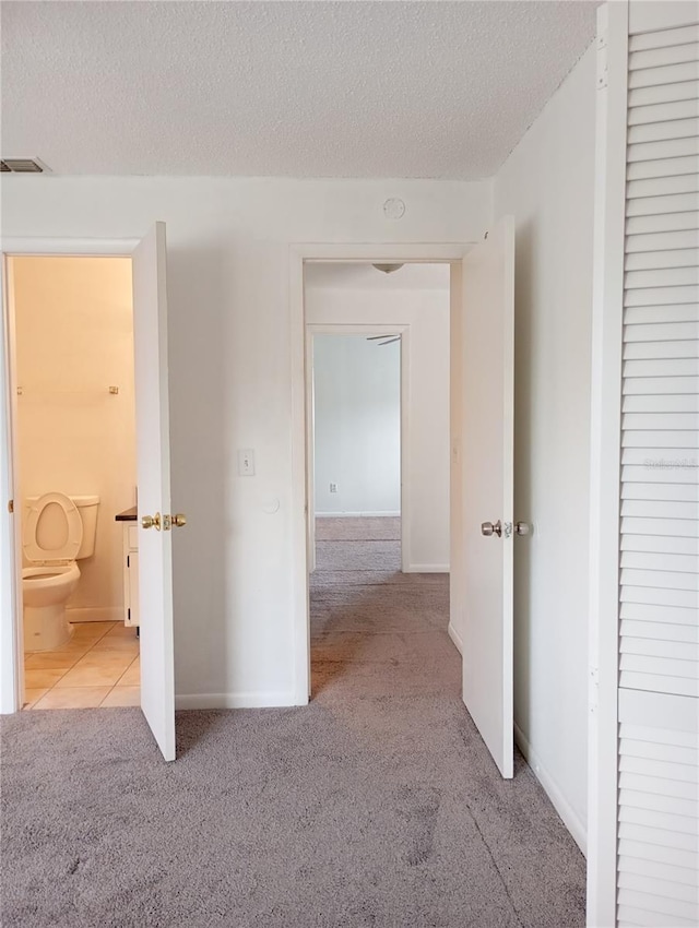 hallway with carpet floors, visible vents, a textured ceiling, and baseboards