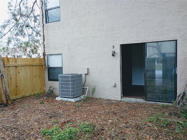 view of exterior entry with stucco siding, fence, and central air condition unit