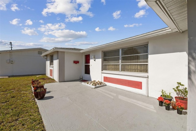 view of exterior entry featuring a lawn, a patio, and stucco siding