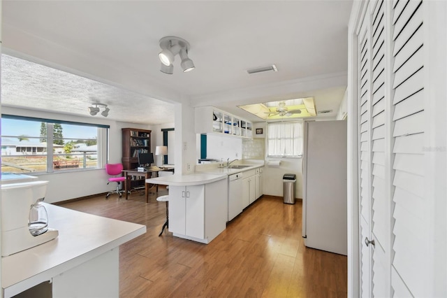 kitchen with light wood-style flooring, decorative backsplash, white appliances, a peninsula, and a kitchen bar