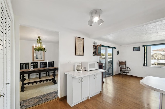 kitchen with light countertops, white microwave, wood finished floors, and baseboards