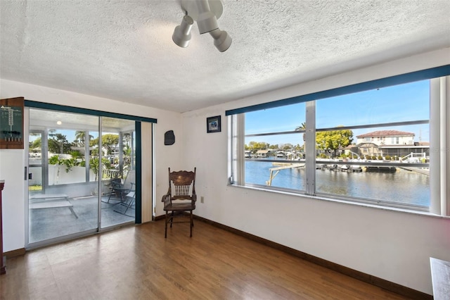 unfurnished room featuring baseboards, a ceiling fan, wood finished floors, a water view, and a textured ceiling