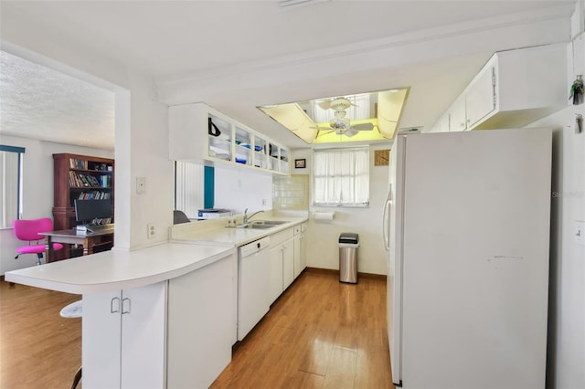 kitchen featuring light countertops, a sink, light wood-type flooring, white appliances, and a peninsula