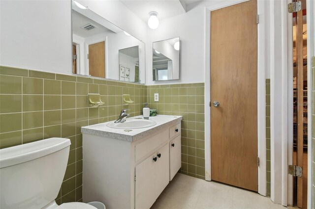 bathroom featuring visible vents, toilet, tile patterned floors, vanity, and tile walls