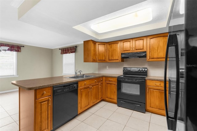 kitchen featuring under cabinet range hood, a peninsula, brown cabinetry, black appliances, and a sink