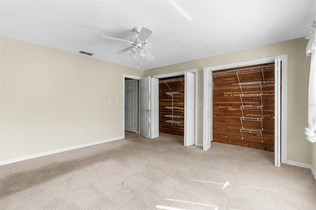 unfurnished bedroom with visible vents, two closets, baseboards, and carpet floors