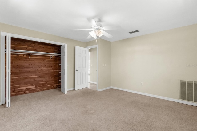 unfurnished bedroom featuring a closet, visible vents, light colored carpet, and wood walls