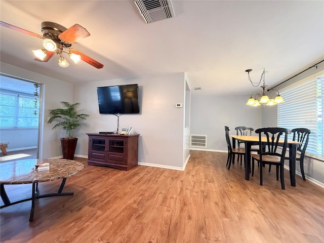 living room featuring light wood-style floors, visible vents, baseboards, and ceiling fan with notable chandelier