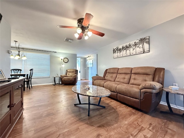 living area with ceiling fan with notable chandelier, wood finished floors, visible vents, and baseboards
