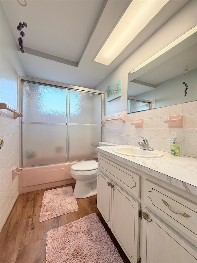 full bathroom with toilet, shower / bath combination with glass door, wood finished floors, vanity, and tile walls