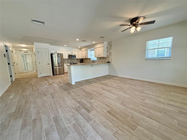 kitchen with stainless steel appliances, visible vents, backsplash, open floor plan, and light wood-type flooring