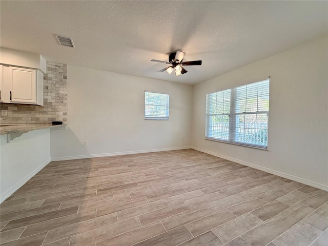 spare room with light wood finished floors, baseboards, visible vents, a ceiling fan, and a textured ceiling