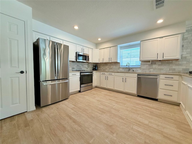 kitchen with appliances with stainless steel finishes, light wood-type flooring, visible vents, and a sink