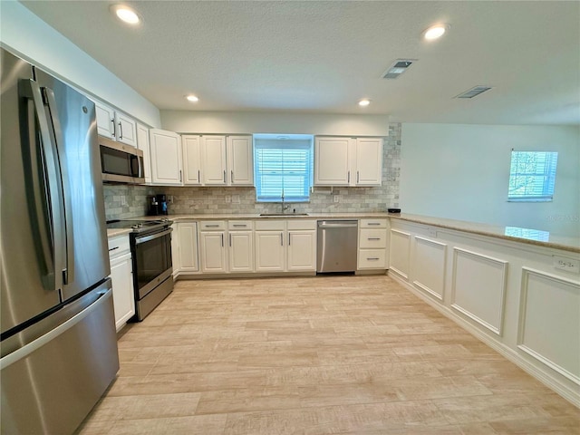 kitchen featuring light wood finished floors, tasteful backsplash, light countertops, appliances with stainless steel finishes, and a sink