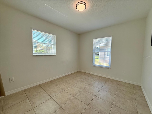 spare room with a textured ceiling, light tile patterned flooring, and baseboards