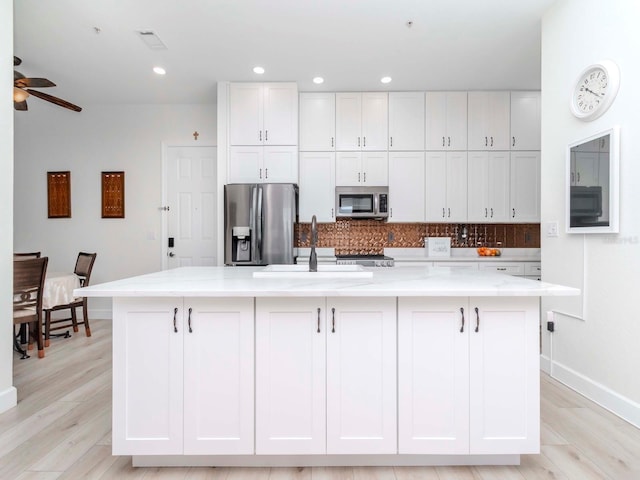 kitchen featuring a center island with sink, a sink, appliances with stainless steel finishes, white cabinetry, and light wood-type flooring