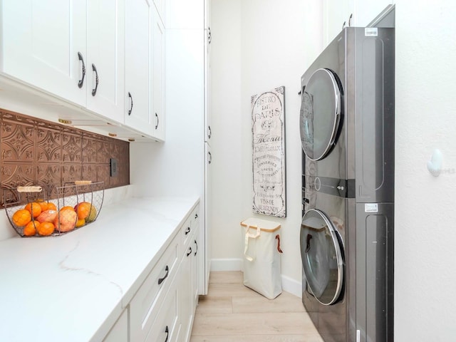 clothes washing area featuring baseboards, cabinet space, stacked washer and clothes dryer, and light wood-style floors