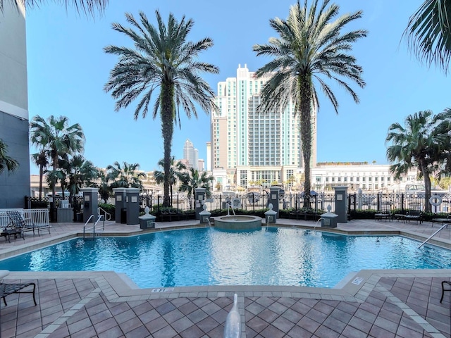 view of pool featuring a patio area, fence, a pool with connected hot tub, and a city view