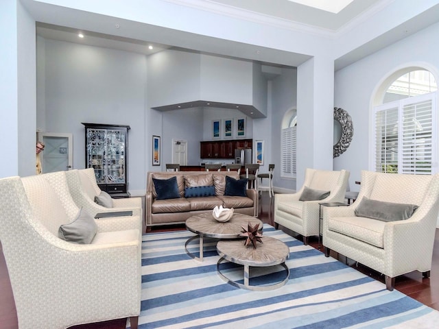 living area with baseboards, a high ceiling, ornamental molding, and wood finished floors