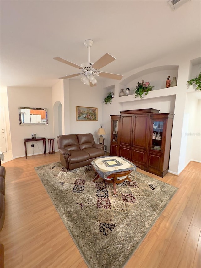 living room with light wood-type flooring, arched walkways, ceiling fan, and built in features