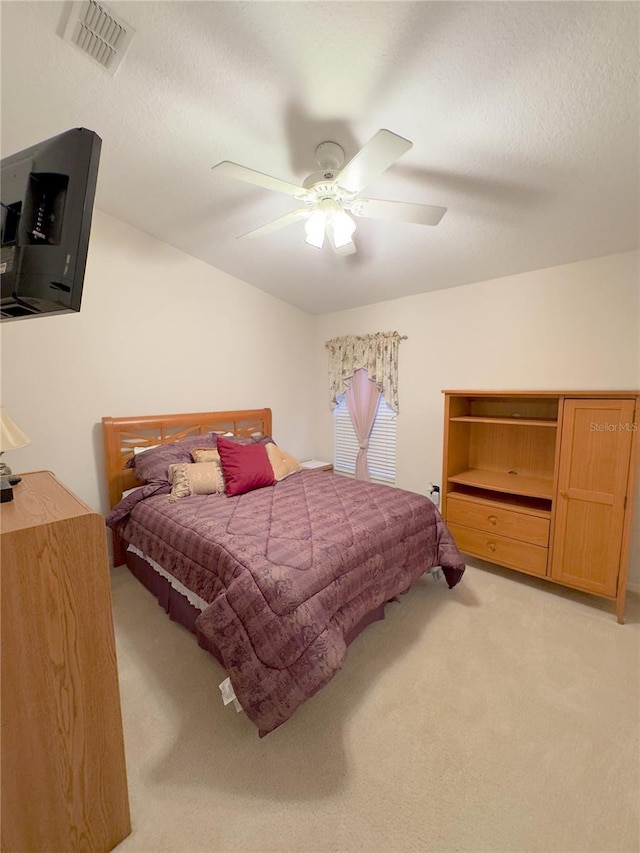 bedroom featuring light carpet, ceiling fan, visible vents, and a textured ceiling