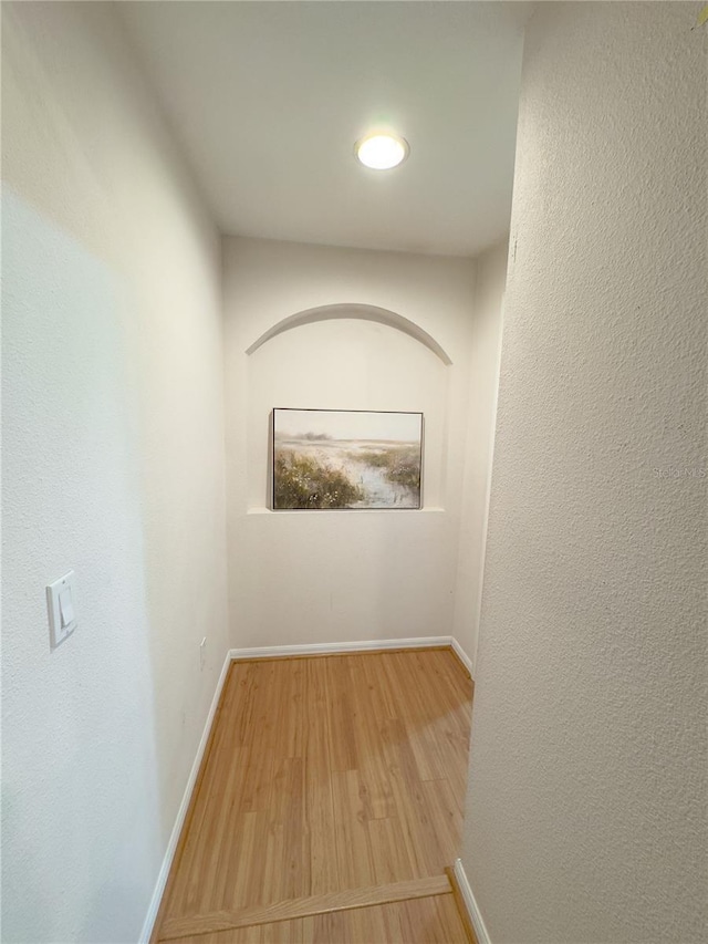 hallway featuring a textured wall, baseboards, and wood finished floors