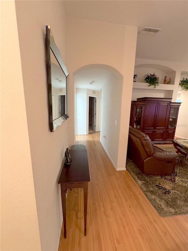 hall featuring baseboards, visible vents, arched walkways, light wood-style floors, and built in shelves