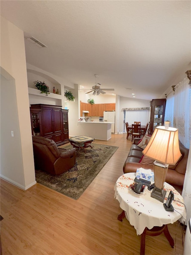 living room featuring lofted ceiling, ceiling fan, visible vents, and light wood-style floors