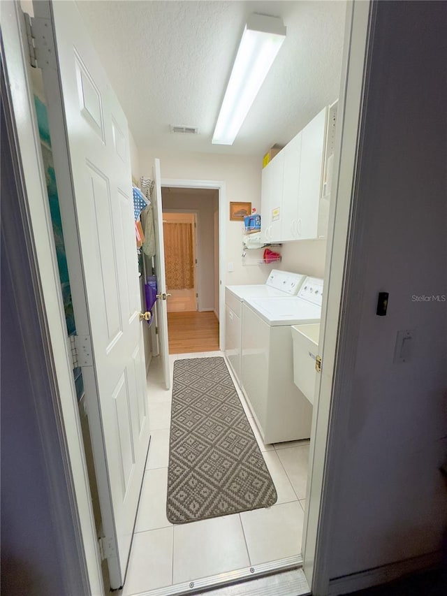 laundry area featuring light tile patterned floors, a textured ceiling, visible vents, washer and dryer, and cabinet space