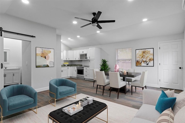 living room featuring lofted ceiling, recessed lighting, a barn door, wood finished floors, and baseboards