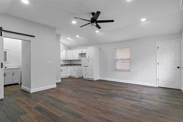 unfurnished living room featuring dark wood-style flooring, recessed lighting, a barn door, ceiling fan, and vaulted ceiling