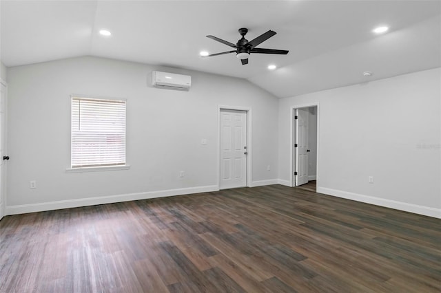 spare room featuring vaulted ceiling, a wall unit AC, dark wood-style floors, and baseboards