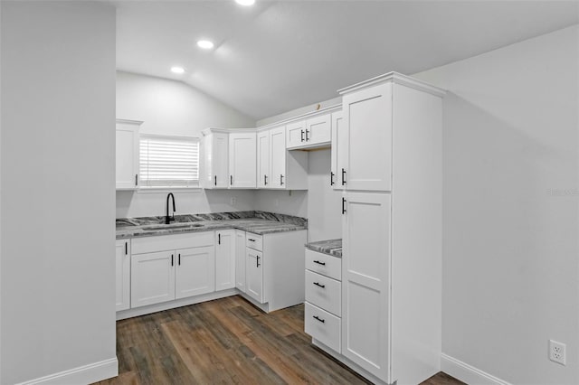 kitchen with light stone counters, dark wood-style flooring, white cabinets, vaulted ceiling, and a sink