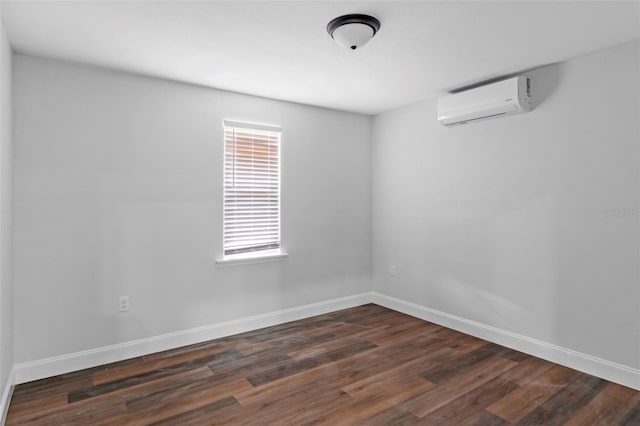 spare room featuring dark wood-style floors, an AC wall unit, and baseboards