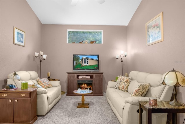 living area with carpet, vaulted ceiling, ceiling fan, and a lit fireplace